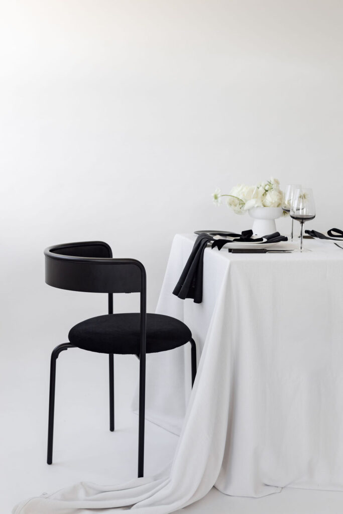 A Christmas table setting with white tablecloth and white flowers & one black chairs on left side from hire society