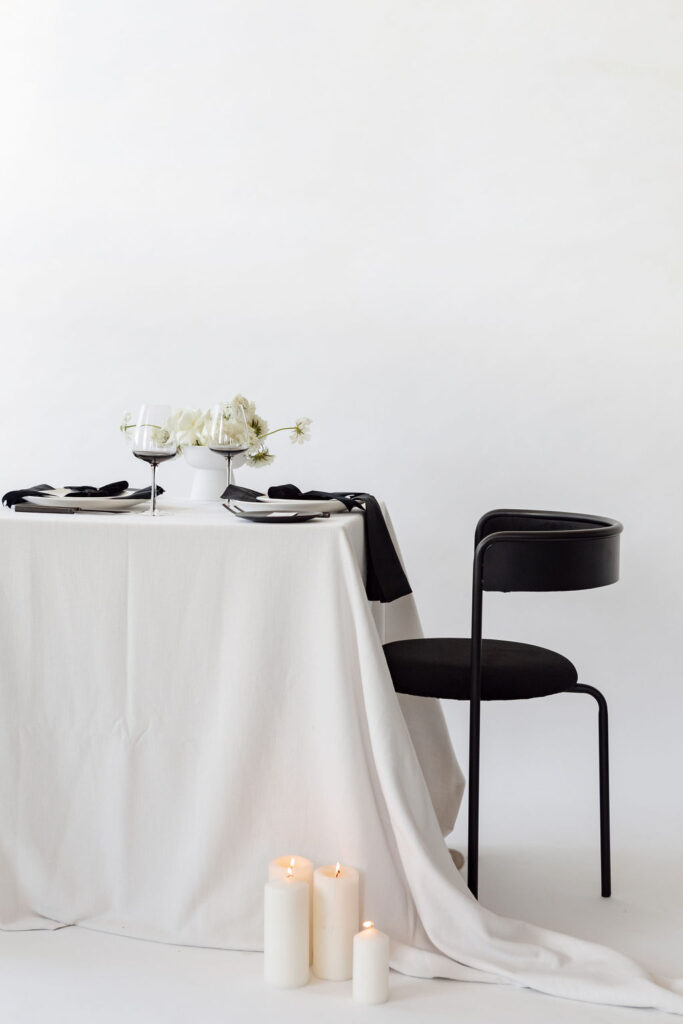 A Christmas table setting with white tablecloth and white flowers & one black chairs on right side from hire society