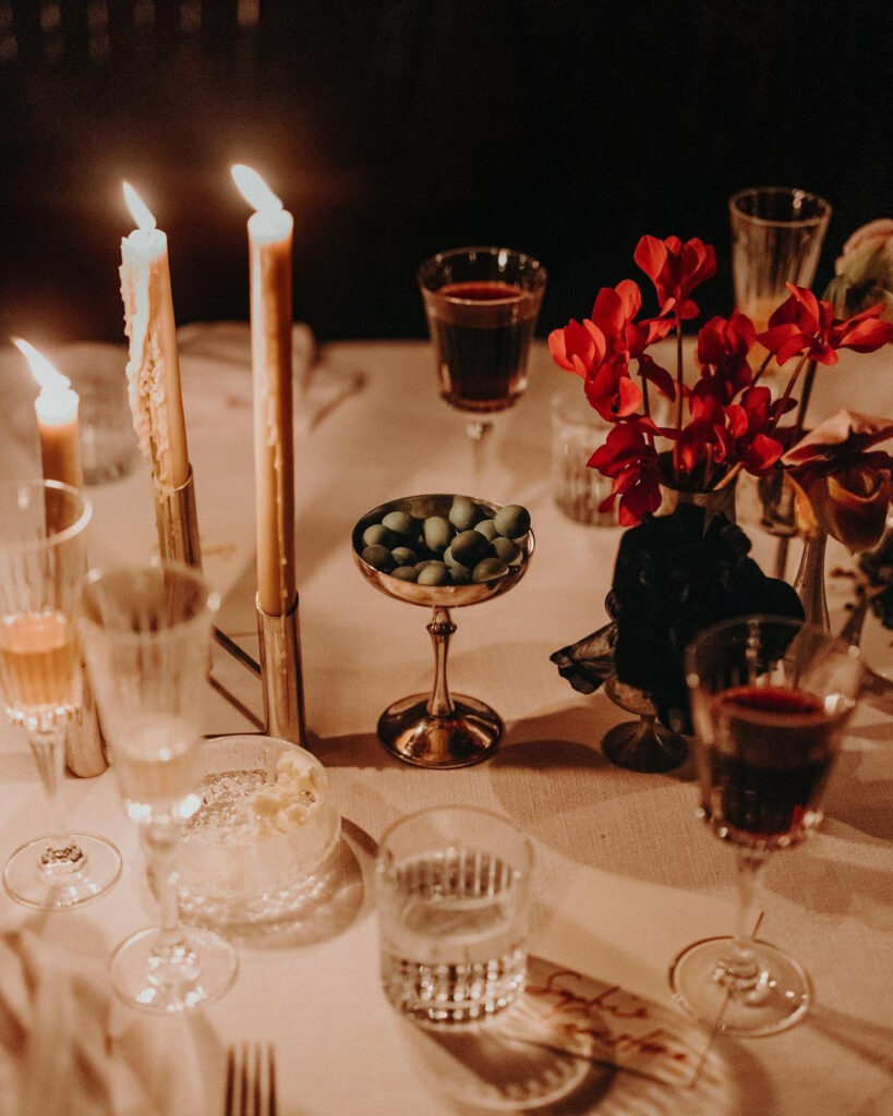Close up of an ambient, candlelit winter wedding table with red flowers and olives