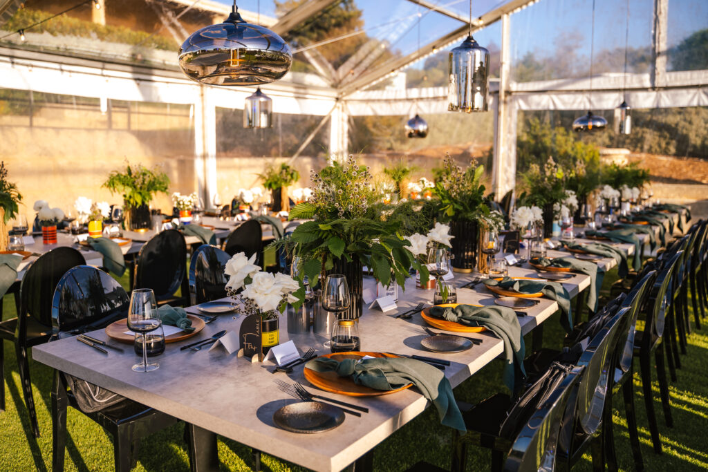 Close up of outdoor table setting for featuring black chairs, green linen napkins and leafy table arrangements