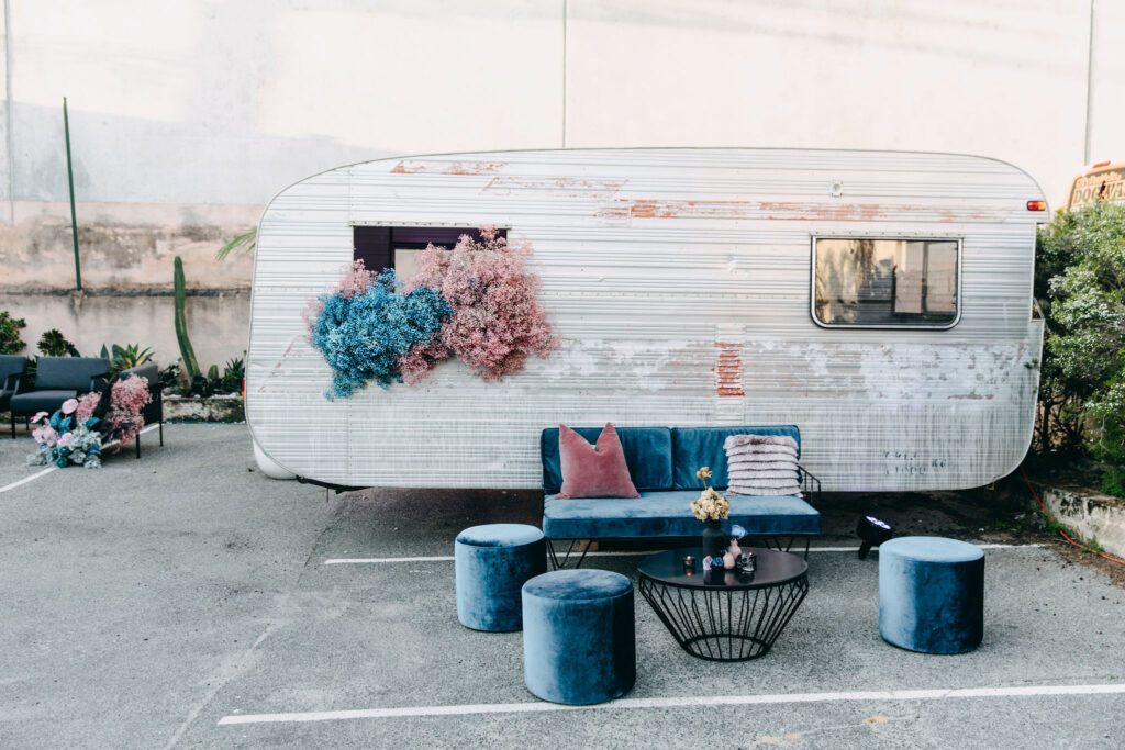 Blue velvet seating, and pink and blue flower installation in front of a campervan